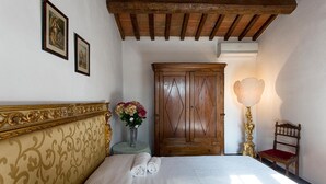 Ein Schlafzimmer mit einem großen Bett, einem Holzschrank, einem kleinen Tisch mit Blumenvase und einem Stuhl.
