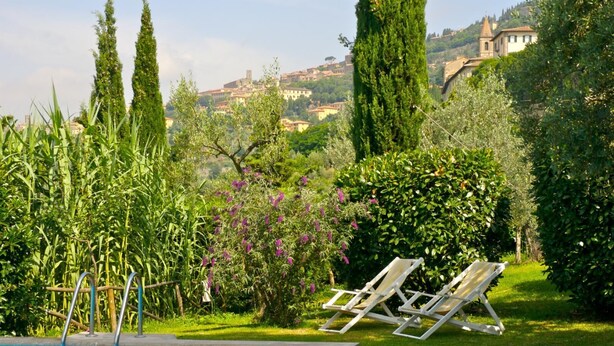Una piscina con dos sillas de descanso, rodeada de vegetación y vistas a un pueblo en la ladera.