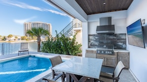 A modern outdoor kitchen with a pool, dining area, and a view of a cityscape. - Lake Views ~ Private Pool ~ Outdoor Lounge Area (Destin)
