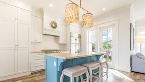 A kitchen with white cabinets, a blue island, two barstools, and a chandelier. - Lake Views ~ Private Pool ~ Outdoor Lounge Area (Destin)