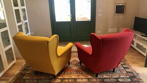 Une pièce comprenant deux fauteuils, un tapis à motifs, un téléviseur et un meuble avec des portes en verre.