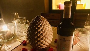 Une bouteille de vin Tenute Oresti, un centre de table en forme de pomme de pin et des verres à vin sur une table éclairée par une bougie.
