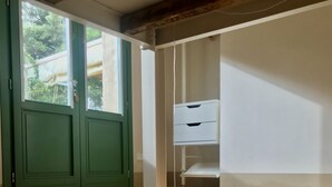 Une chambre à coucher avec un lit, une fenêtre avec des volets verts, un bureau avec des tiroirs et un luminaire suspendu.