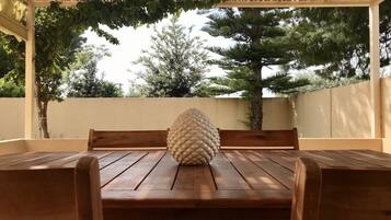 A wooden table with a textured spherical object in the center, surrounded by wooden chairs, set against a backdrop of trees and a white wall.