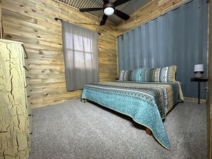 A bedroom with a bed, curtains, a ceiling fan, and a lamp.