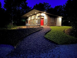 A modern house with a gravel driveway leading to a red door, surrounded by a well-maintained lawn and trees.