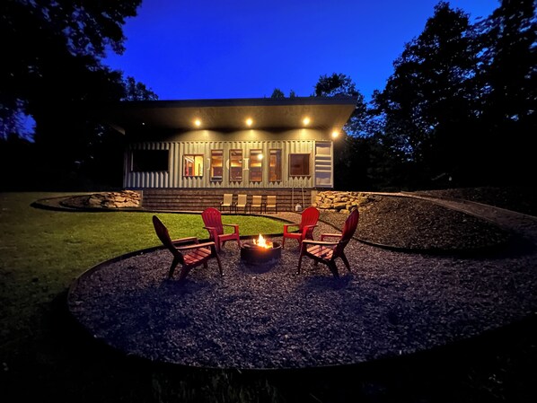 A cozy outdoor seating area with a fire pit and chairs, surrounded by a well-maintained lawn and a stone wall.