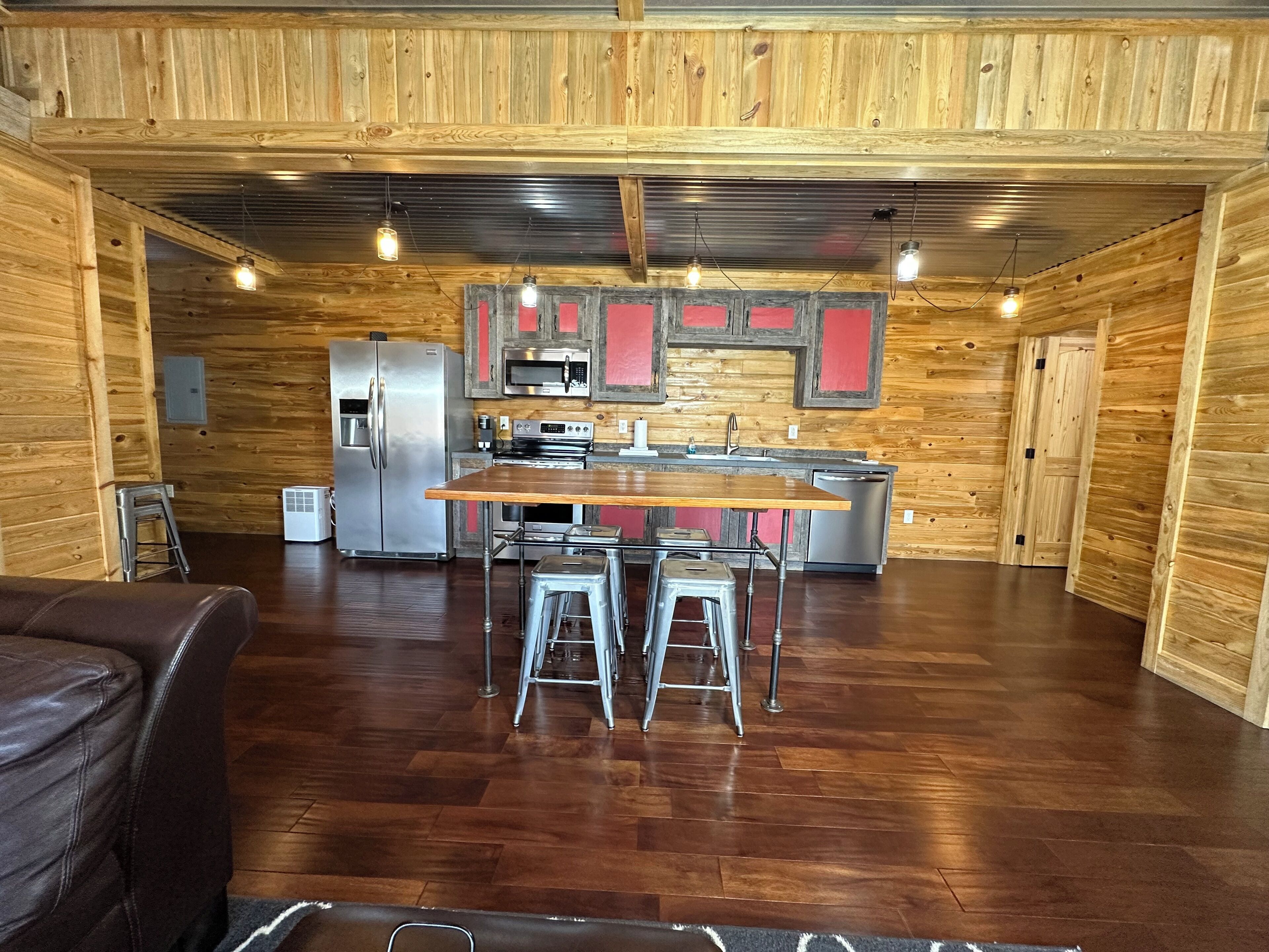 A spacious kitchen with wooden walls, a central island with stools, stainless steel appliances, and pendant lighting.