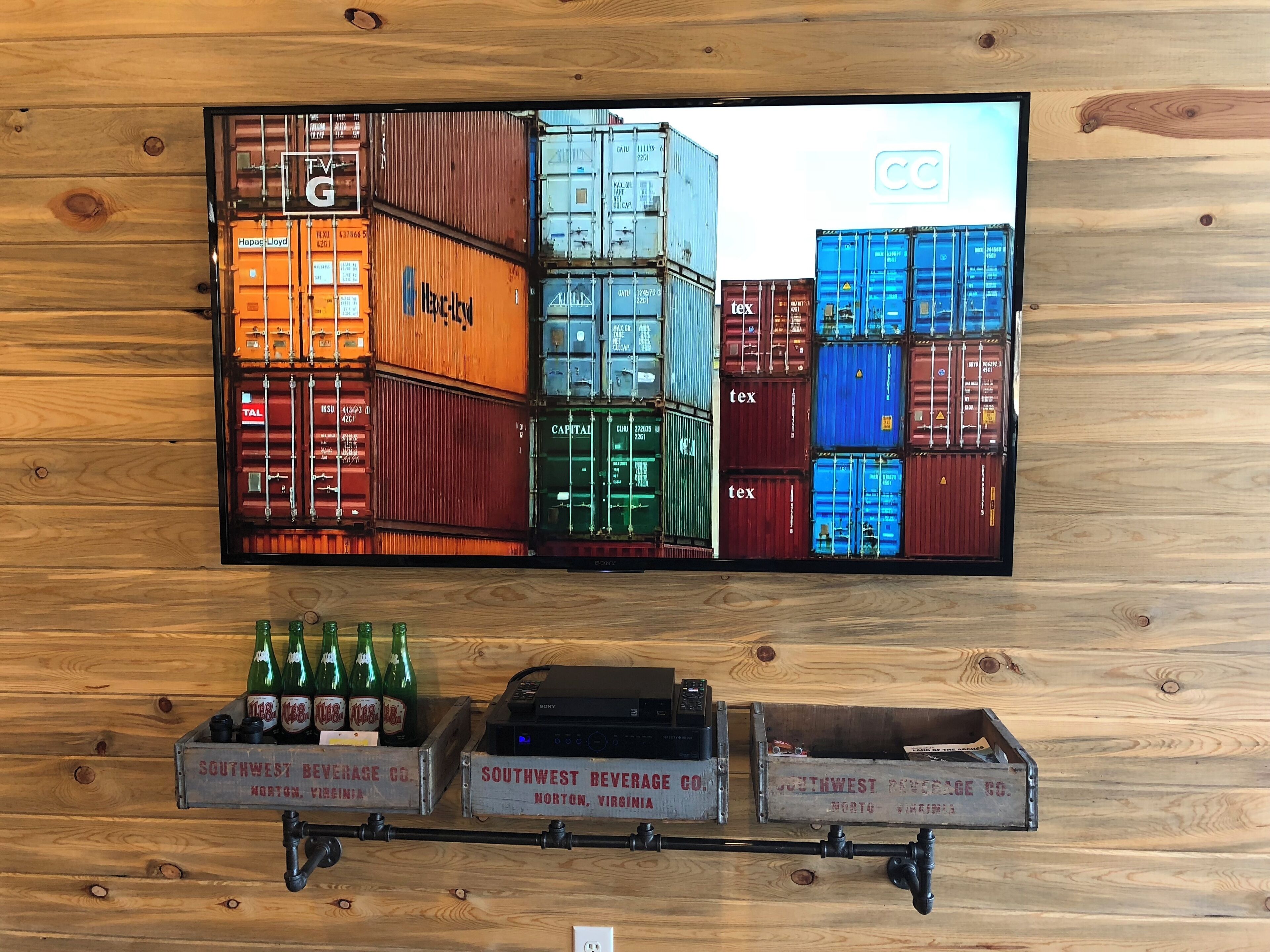 Una pared con un televisor que muestra contenedores de envío de colores y tres cajas antiguas con la etiqueta 'Southwest Beverage Co.'