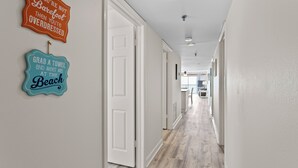 Een gang met witte muren en houten vloeren, die leidt naar een kamer met een plafondlamp.
