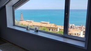 Una habitación con un ventanal grande con vistas a la costa, una cama y una pequeña mesa con dos tazas.