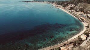 Vista aérea de un pueblo costero con mar azul cristalino, una playa arenosa y una vía ferroviaria que recorre la costa.