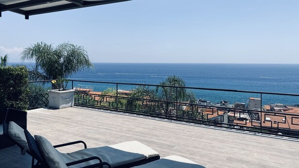 Un balcón con vista al mar, una silla de descanso y una planta en maceta.