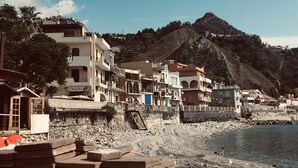 Un pueblo costero con edificios a lo largo del paseo marítimo, una playa rocosa y una montaña al fondo.