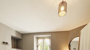 Ein Schlafzimmer mit Bett, Fenster, Kamin und einer Pendelleuchte.