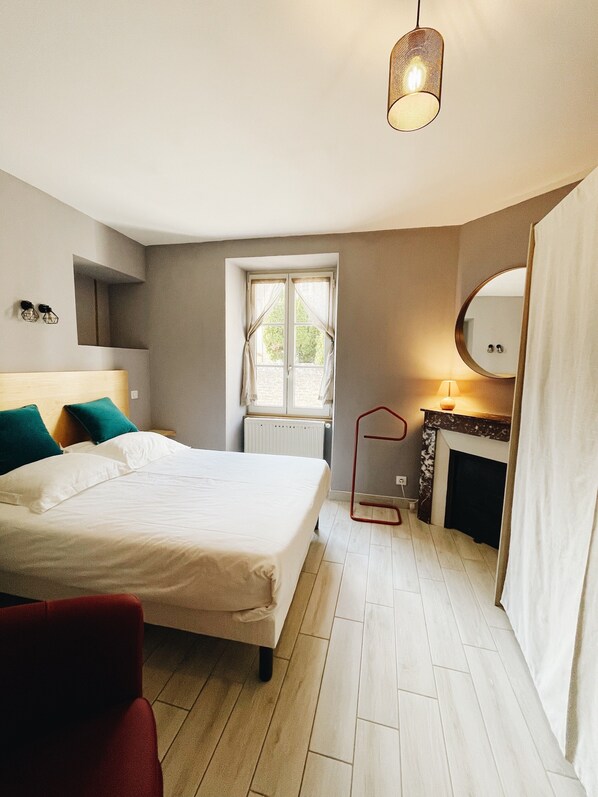A bedroom with a bed, a window, a fireplace, and a hanging light fixture. - Les Hautes Cornières - Apartment (Santenay)