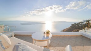 Une terrasse avec une table ronde et deux chaises, offrant une vue sur la côte, avec un plan d’eau et une étendue de terre visible au loin.