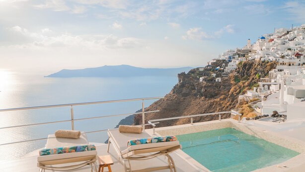 Un espace aménagé au bord de la piscine, avec des chaises longues et une vue sur une ville côtière aux bâtiments blancs.