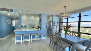 Uma cozinha moderna com armários brancos, uma ilha central com banquetas e uma área de refeições com mesa e cadeiras.