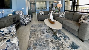 Uma sala de estar moderna com um sofá cinzento, um banquinho estampado e uma mesa de centro redonda com um objeto decorativo.