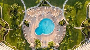 Vista aérea de um resort com uma piscina central cercada por áreas de descanso e palmeiras.