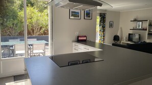 A modern kitchen with a large island, a dining area with a glass table, and a view of greenery outside.