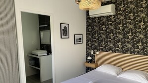 A bedroom with a bed, a nightstand, a wall-mounted air conditioner, and a bathroom visible through an open door.