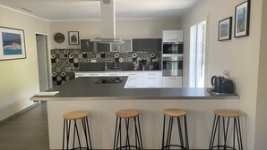 A modern kitchen with a central island, bar stools, and a large window providing natural light.