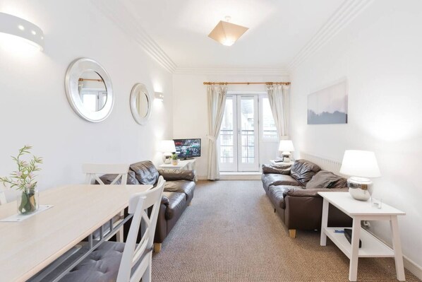 A modern living room with a dining area, featuring a sofa set, a dining table, and a TV.