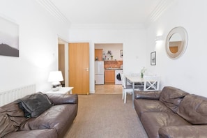 A living room with two brown leather sofas, a white table, and a kitchen in the background.