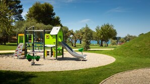 A playground with a slide and climbing structures, surrounded by grass and trees. - "BUENA VISTA" 55m2, south-facing balcony, fenced, 5ft. beach, suitable for children, Rovinj (Rovinj)