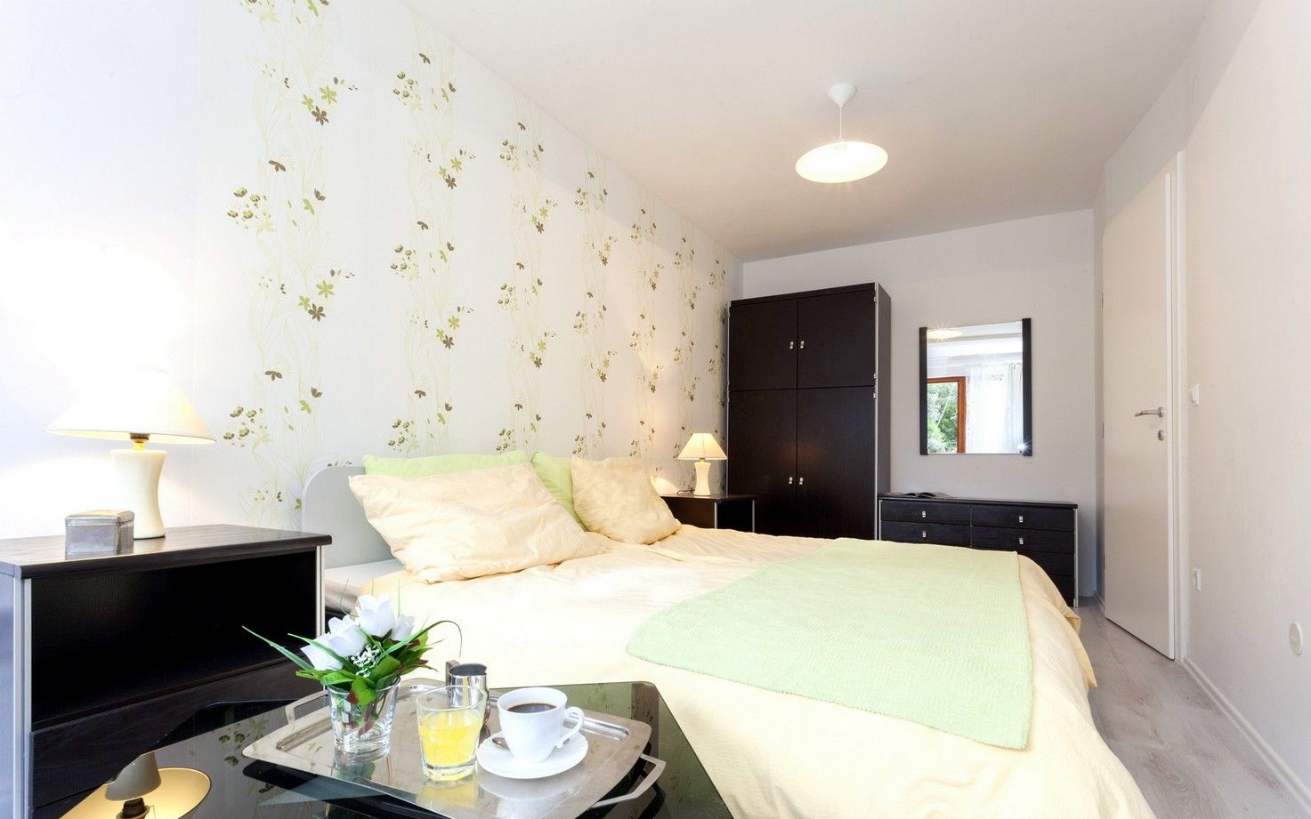 A modern bedroom with a bed, bedside tables, a wardrobe, and a tray with a cup and glass.