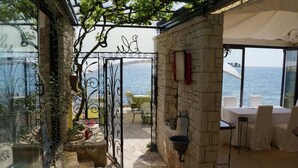 An outdoor seating area with stone walls, a metal gate, and a view of the sea. - "BUENA VISTA" 55m2, south-facing balcony, fenced, 5ft. beach, suitable for children, Rovinj (Rovinj)