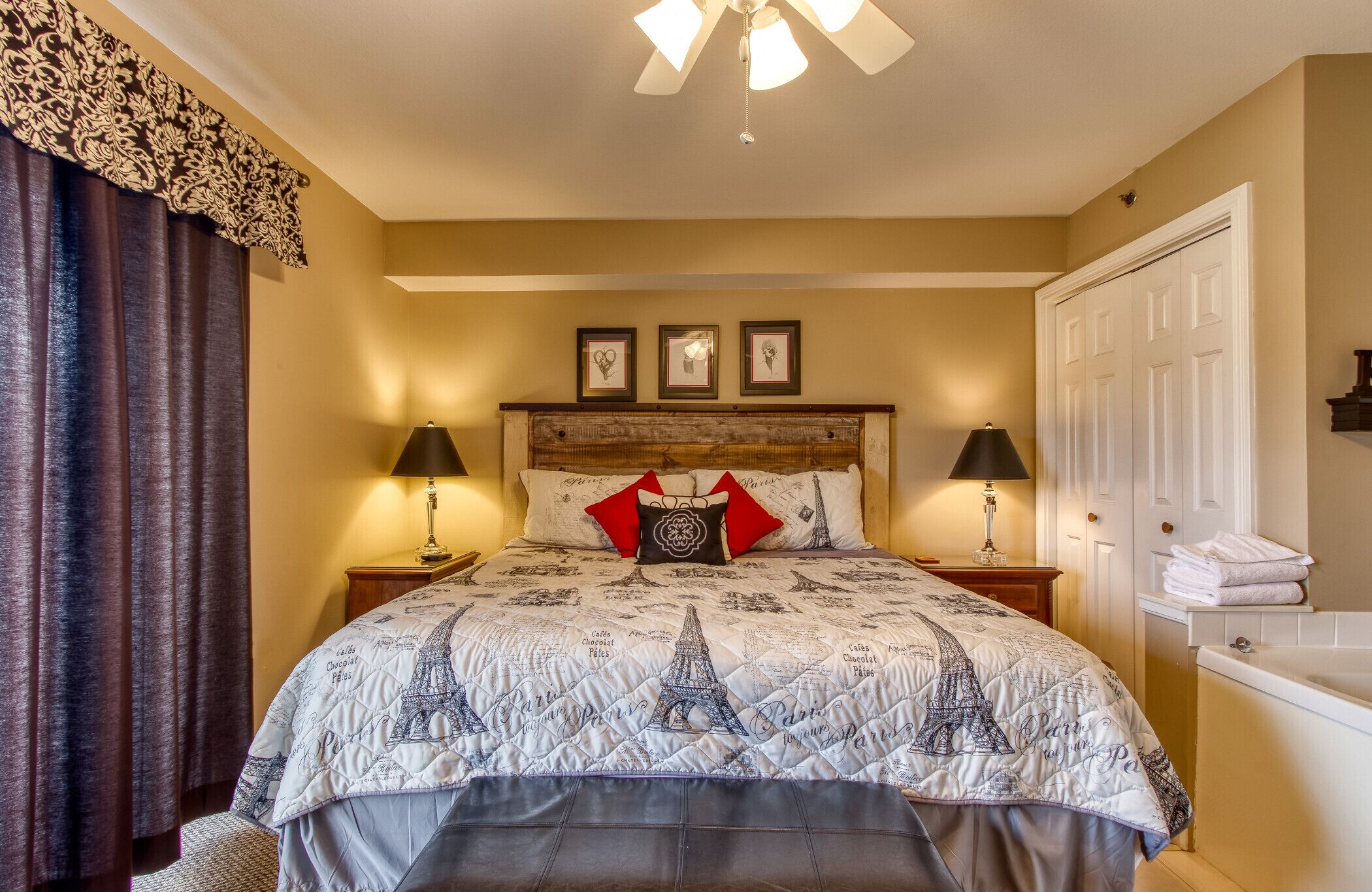 Una habitación de hotel con una cama, un edredón con motivos de París, dos lámparas de noche, un cabecero de madera y una puerta blanca.