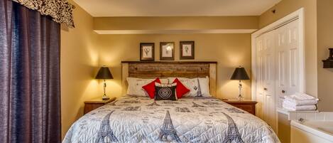 Una habitación de hotel con una cama, un edredón con motivos de París, dos lámparas de noche, un cabecero de madera y una puerta blanca.