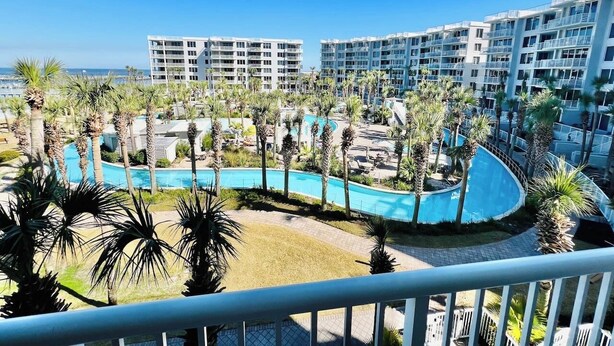 A resort with a curved pool, palm trees, and high-rise buildings in the background. - Heron 408 — 3BR Bayside Condo at Destin West with Heated Pool (Fort Walton Beach)
