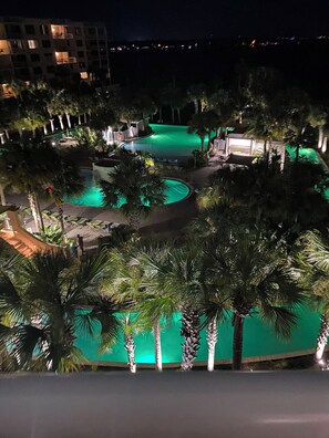 Une vue nocturne d’un complexe hôtelier doté de plusieurs piscines, de palmiers et d’un bâtiment dont les fenêtres sont illuminées.