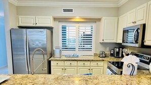 A kitchen with granite countertops, stainless steel appliances, and white cabinetry. - Heron 408 — 3BR Bayside Condo at Destin West with Heated Pool (Fort Walton Beach)