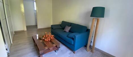 A living room with a blue sofa, a wooden coffee table with orange flowers, and a floor lamp.