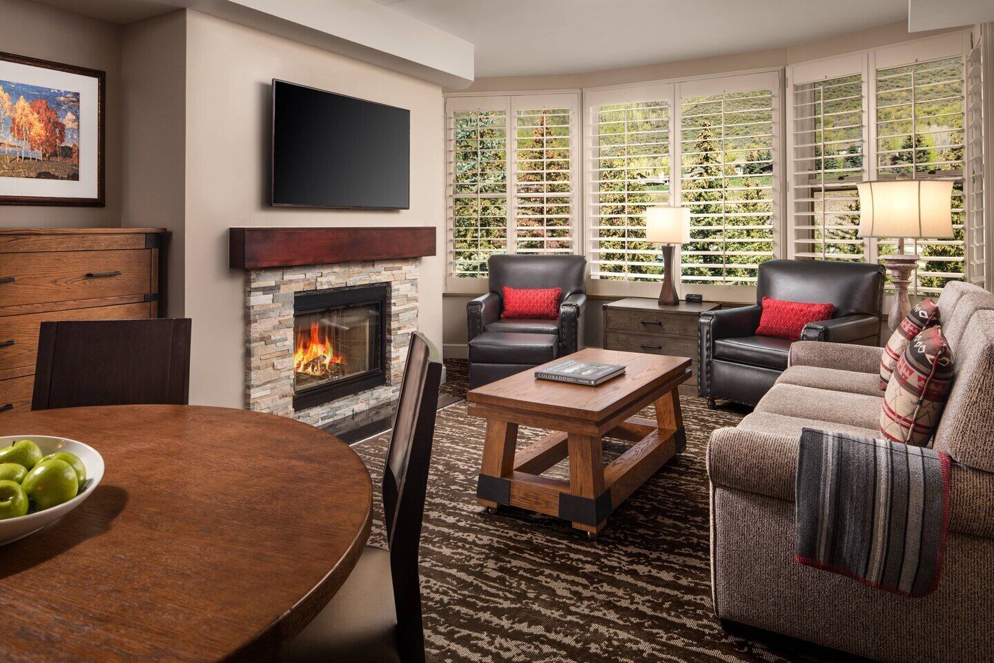 A living room with a fireplace, leather chairs, a coffee table, and a TV mounted on the wall.