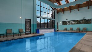 An indoor swimming pool with clear blue water, surrounded by lounge chairs and large windows offering views of the outdoors. - Unit inside a Luxury resort + heated pool (Vail)