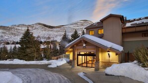 A lodge with a snow-covered entrance, a mountain backdrop, and a clear sky. - Unit inside a Luxury resort + heated pool (Vail)