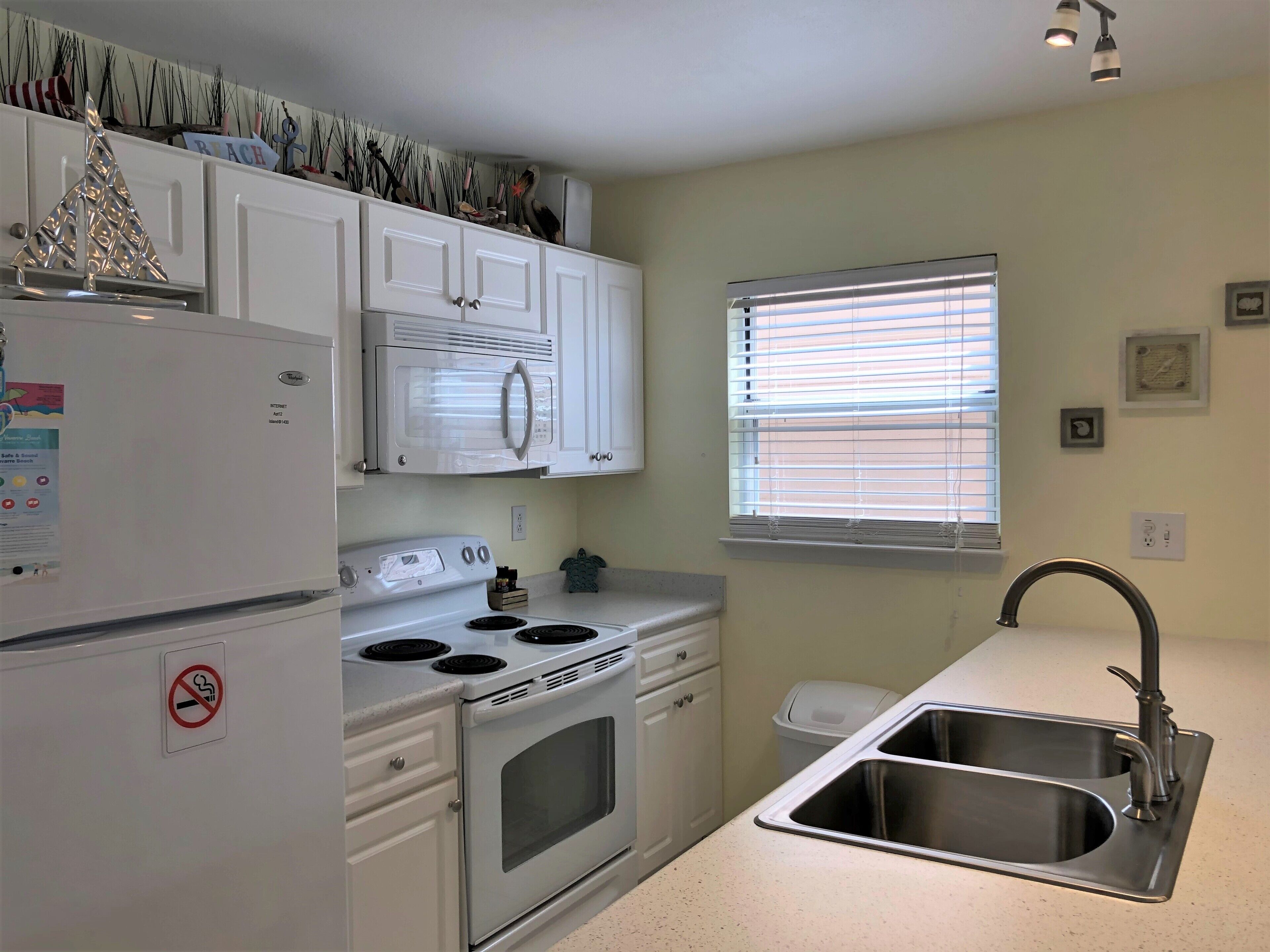 A compact kitchen with white cabinets, a built-in microwave, a stove, and a sink.