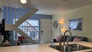 Una cocina con un lavaplatos de acero inoxidable, lavavajillas, una escalera y una puerta que da a un balcón.