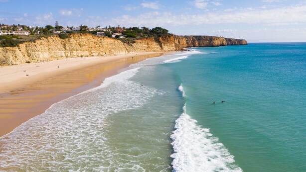 Una playa costera con aguas transparentes, una orilla arenosa y un acantilado con edificios en la cima.