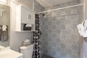 A bathroom with a toilet, a sink, a shower with a patterned curtain, and a towel rack with towels. - Waters Avenue Unit B (Tampa)