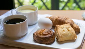 A tray with a croissant, a pastry, a boiled egg, and two cups of coffee.