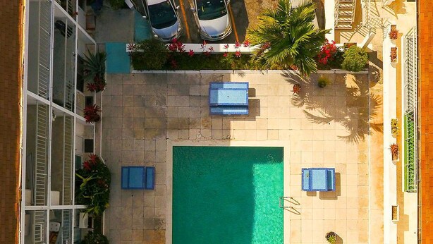 A rooftop swimming pool with four sun loungers, surrounded by potted plants and a building with balconies. - Tangerine Sunsets Seville (Nassau)