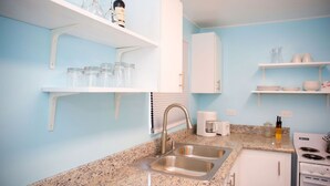 A kitchen with white cabinets, a granite countertop, a stainless steel sink, a coffee maker, and a stove. - Tangerine Sunsets Seville (Nassau)