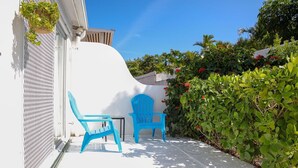 A patio with two blue chairs and a small table, surrounded by lush greenery and a white wall. - Tangerine Sunsets Seville (Nassau)